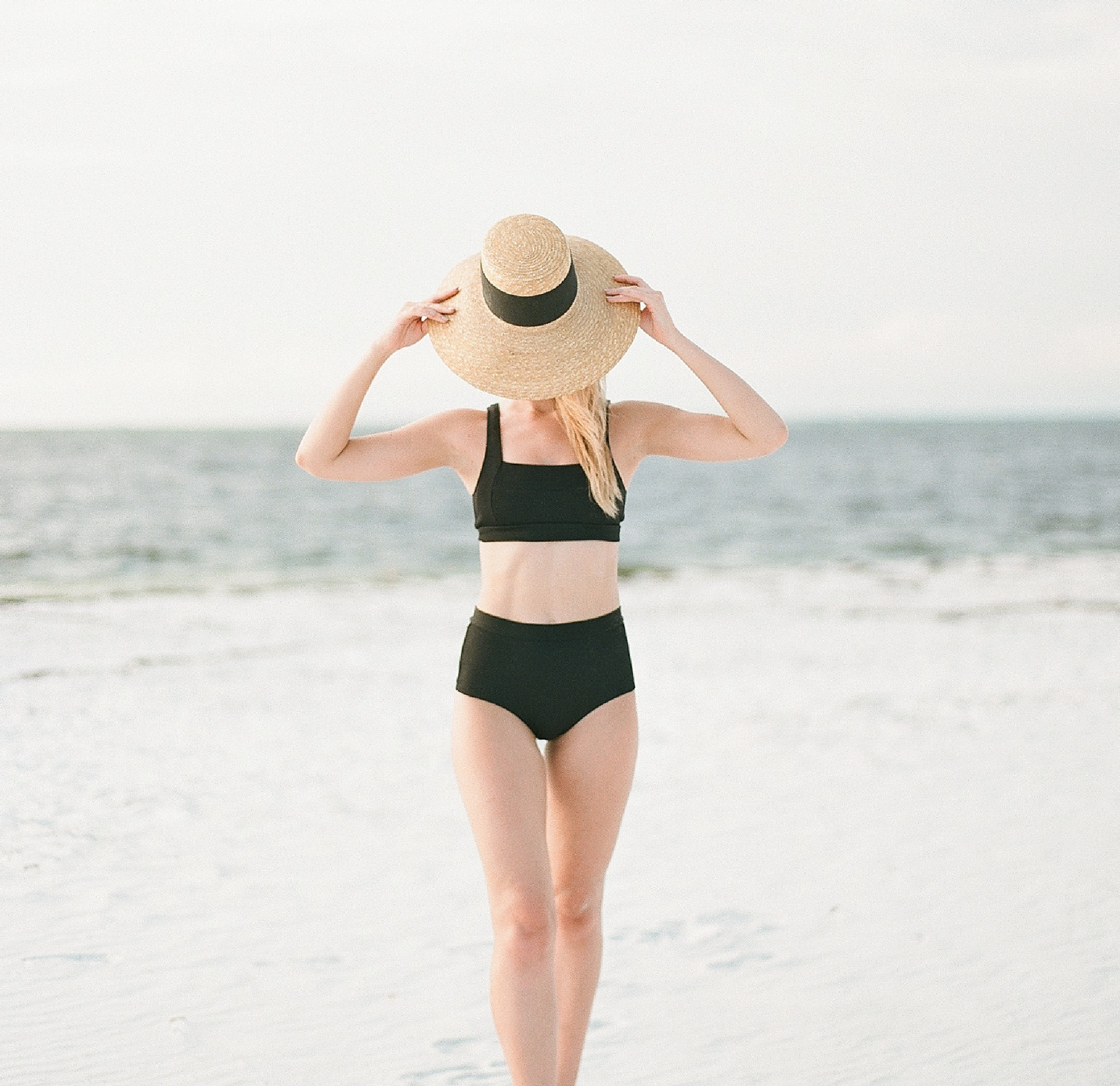 A woman stands confidently on the beach. Beat imposter syndrome with confidence.